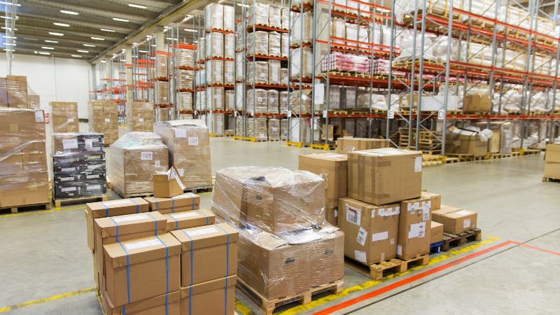 A well-organized warehouse with stacked pallets, packed shelving, and clear floors.