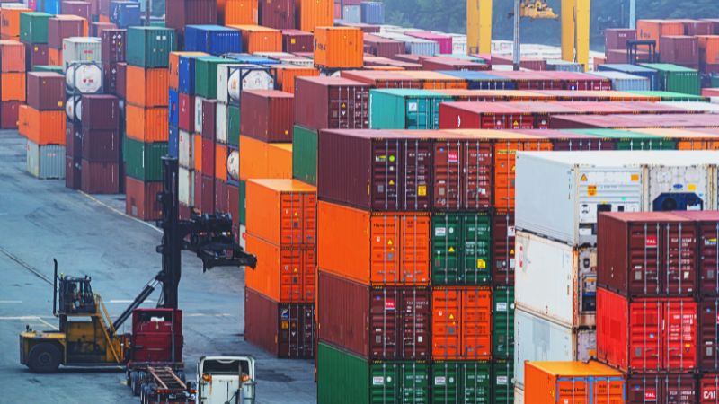 A bustling shipping yard with colorful cargo containers, cranes, and an active forklift.